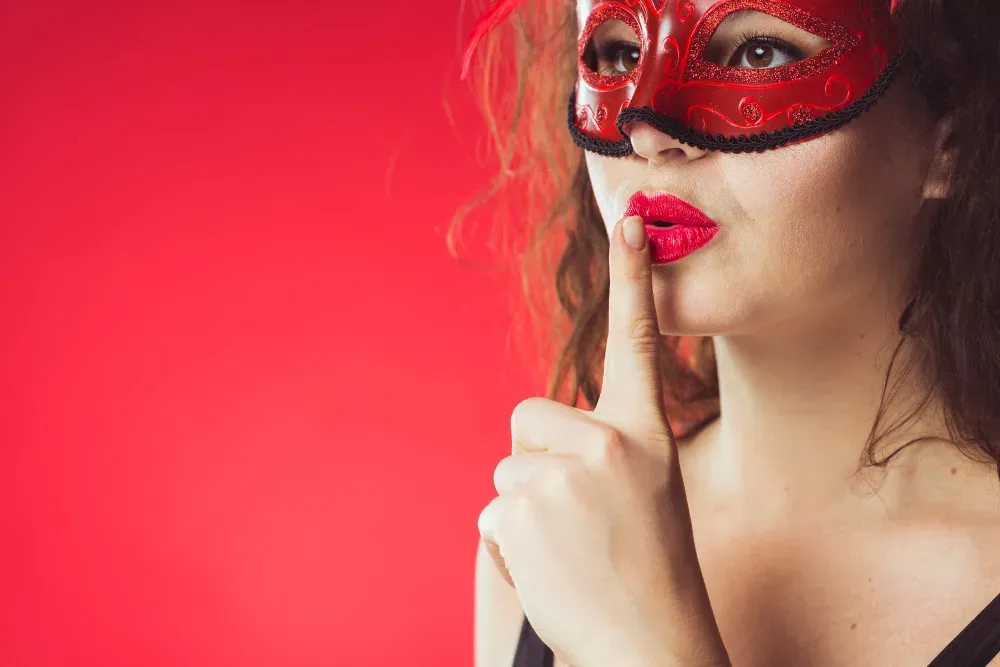 Frau mit roter Maske hält den Finger vor die Lippen