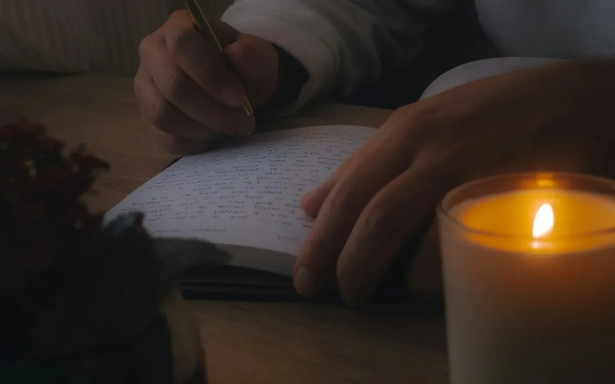 Hände schreiben bei Kerzenlicht in ein Notizbuch