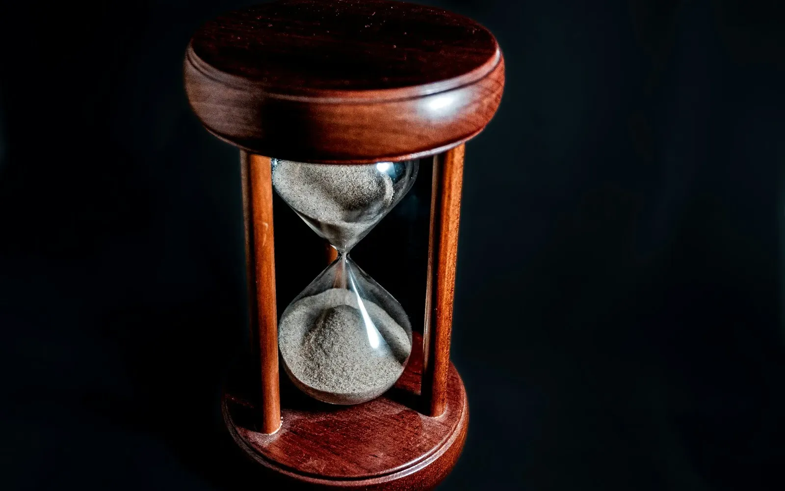 Sanduhr aus Holz und Glas vor schwarzem Hintergrund – Sinnbild für Warten und Verzögern bei Tease and Denial